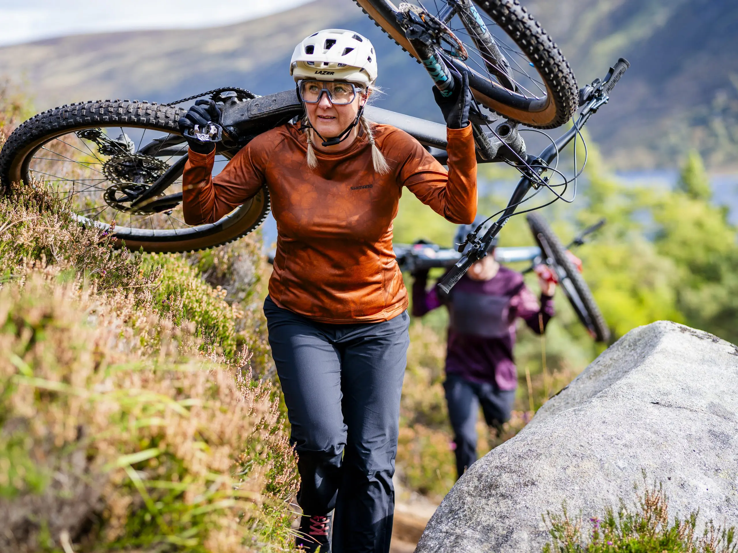 Mountain bike enthusiasts carrying bikes uphill, showcasing outdoor sports marketing, mountain bike event planning, content creation, and logistical support. LOAM.