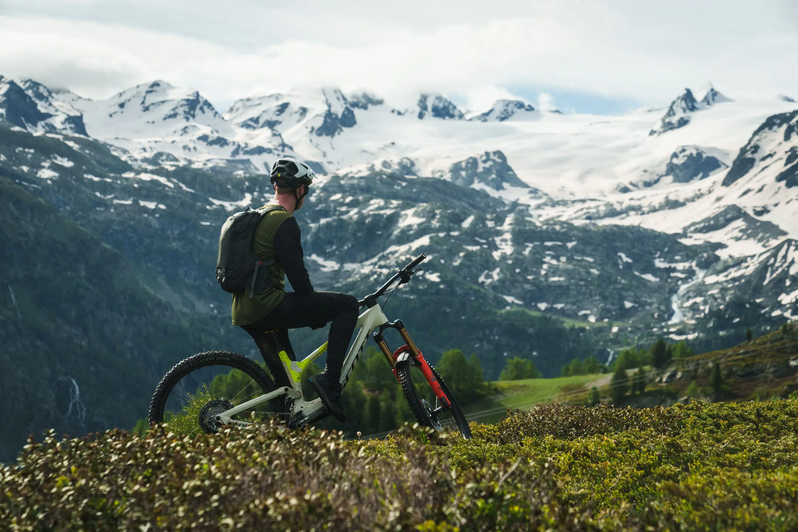Mountain biker overlooks snowy peaks, promoting Mountain Bike Ambassador Management and Marketing Agency in a scenic landscape. LOAM.