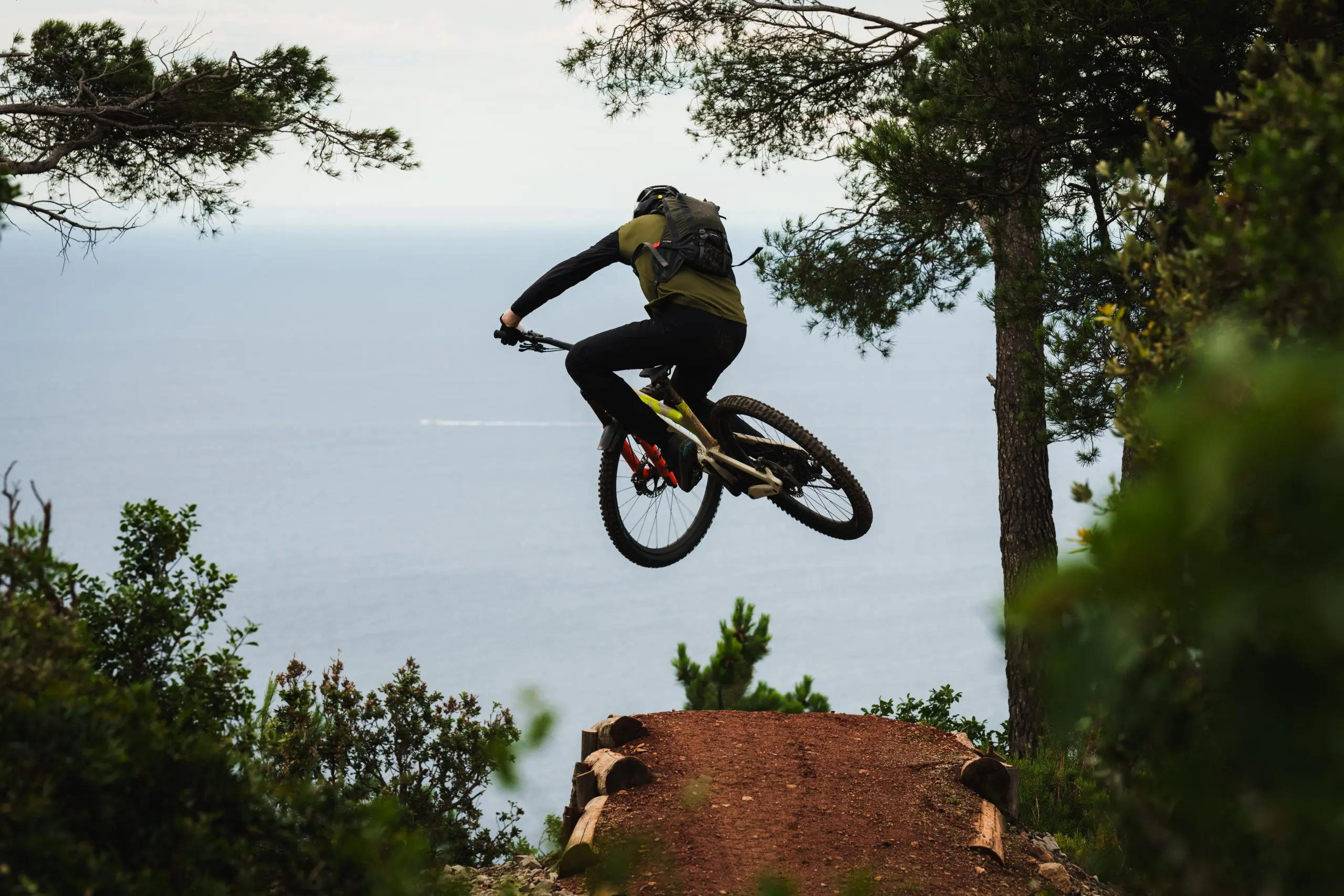 Mountain biker mid-air jump by the sea, showcasing Mountain Bike Ambassador Management, Content Creation, and Event Planning expertise. LOAM.