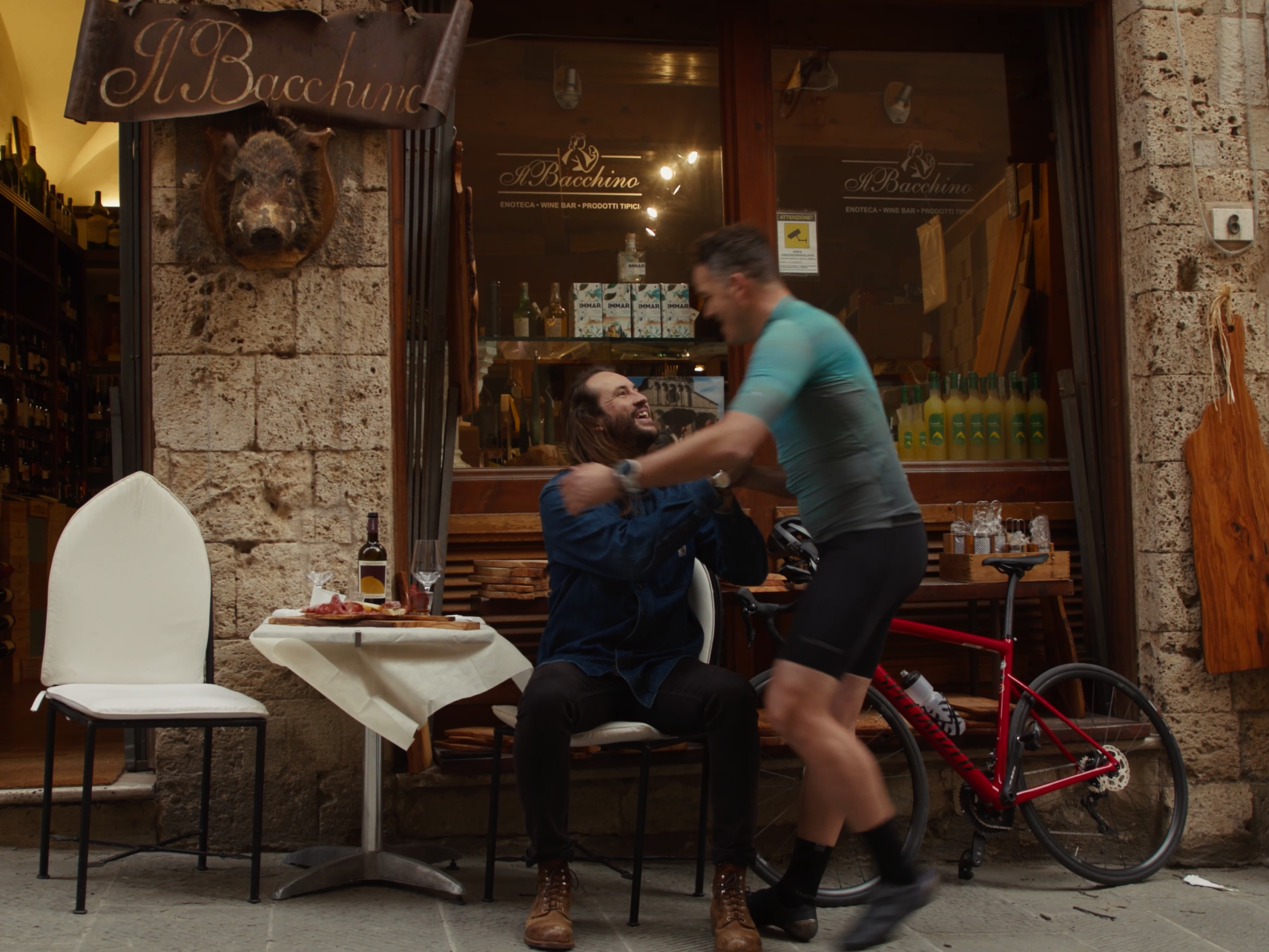 Man greeting a cyclist outside a cafe, bicycles nearby, ideal for Mountain Bike Content Creation and Marketing Agency strategies. LOAM.