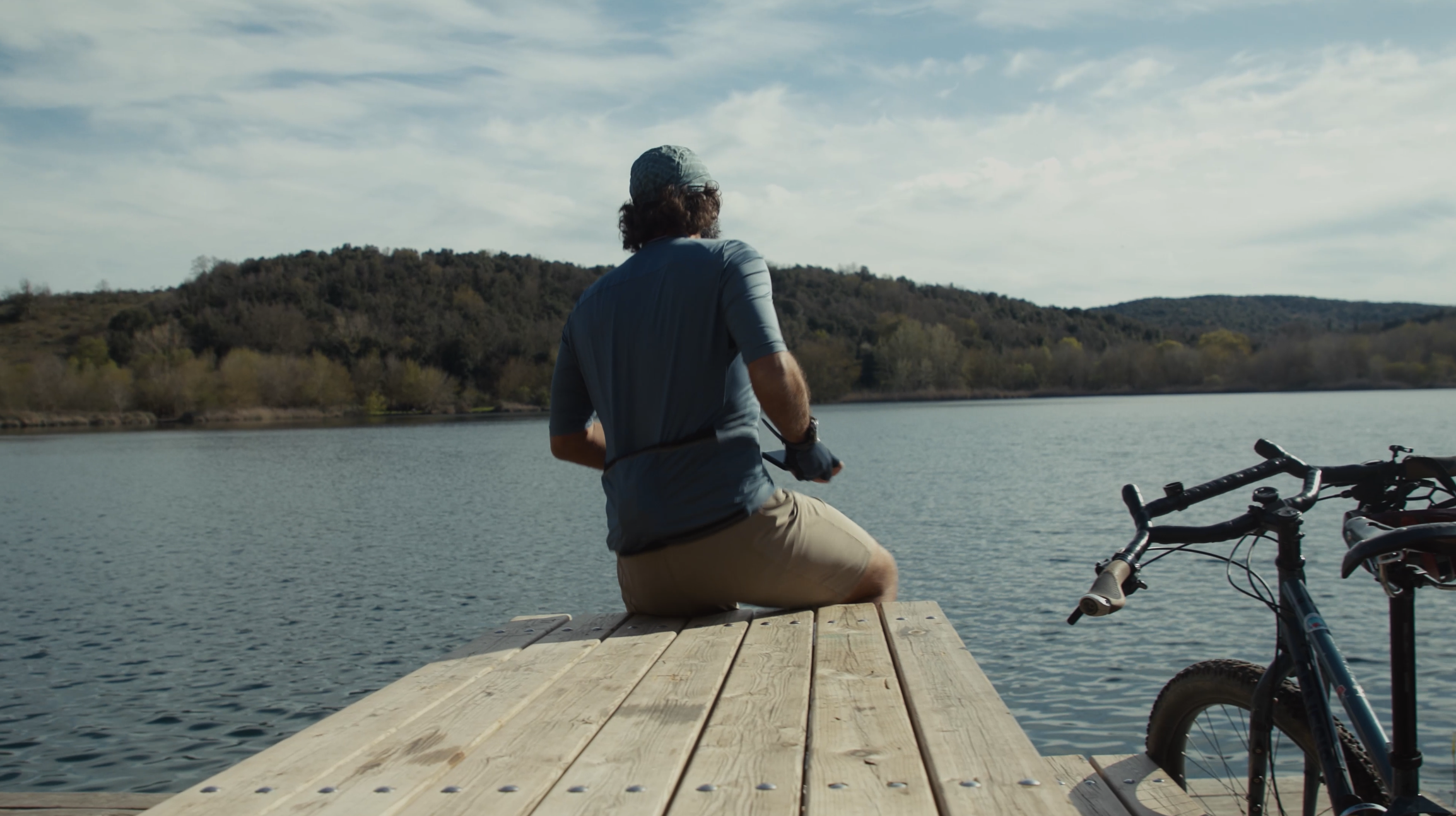 Man sitting on a dock with a mountain bike beside him, ideal for mountain bike content creation and marketing strategy planning. LOAM.