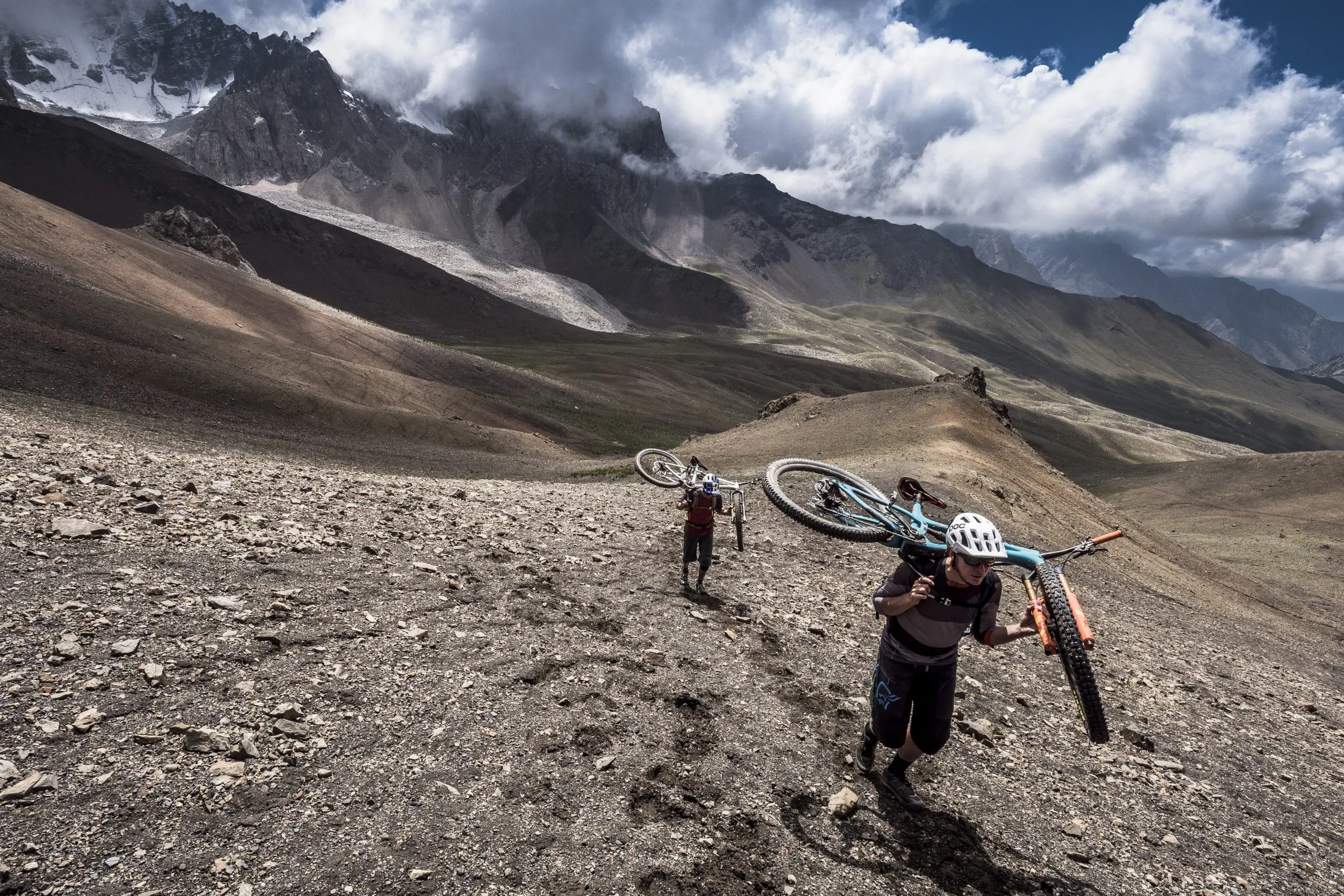 Mountain bikers carry bikes uphill on Euan Wilson's Global Trail Adventures with LOAM. Mountain Bike Content Creation and Event Planner insights. LOAM.