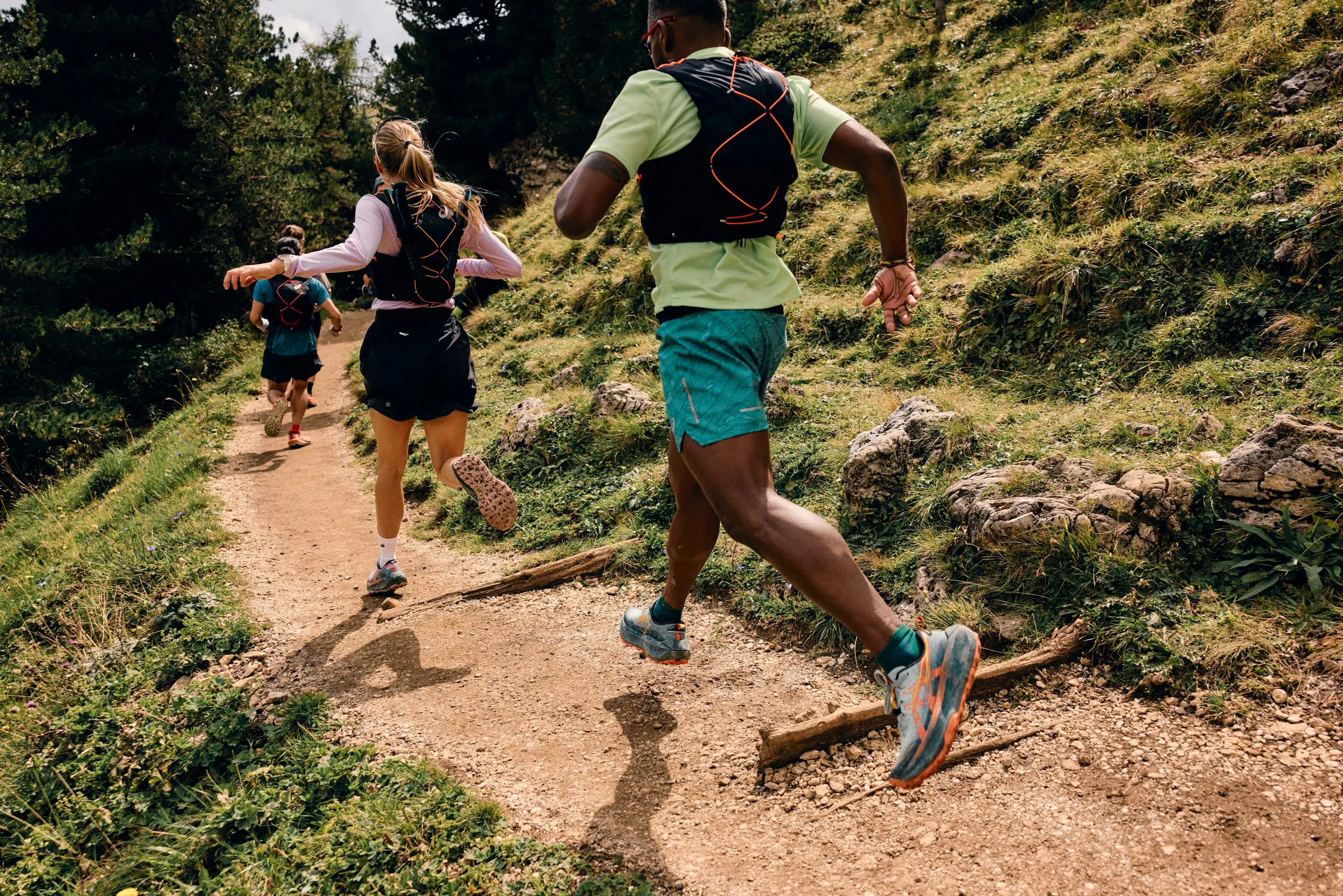 Trail runners in ASICS gear navigate a forest path in the Dolomites, highlighting the ASICS Trail Running Dolomites Campaign and logistical support. LOAM.