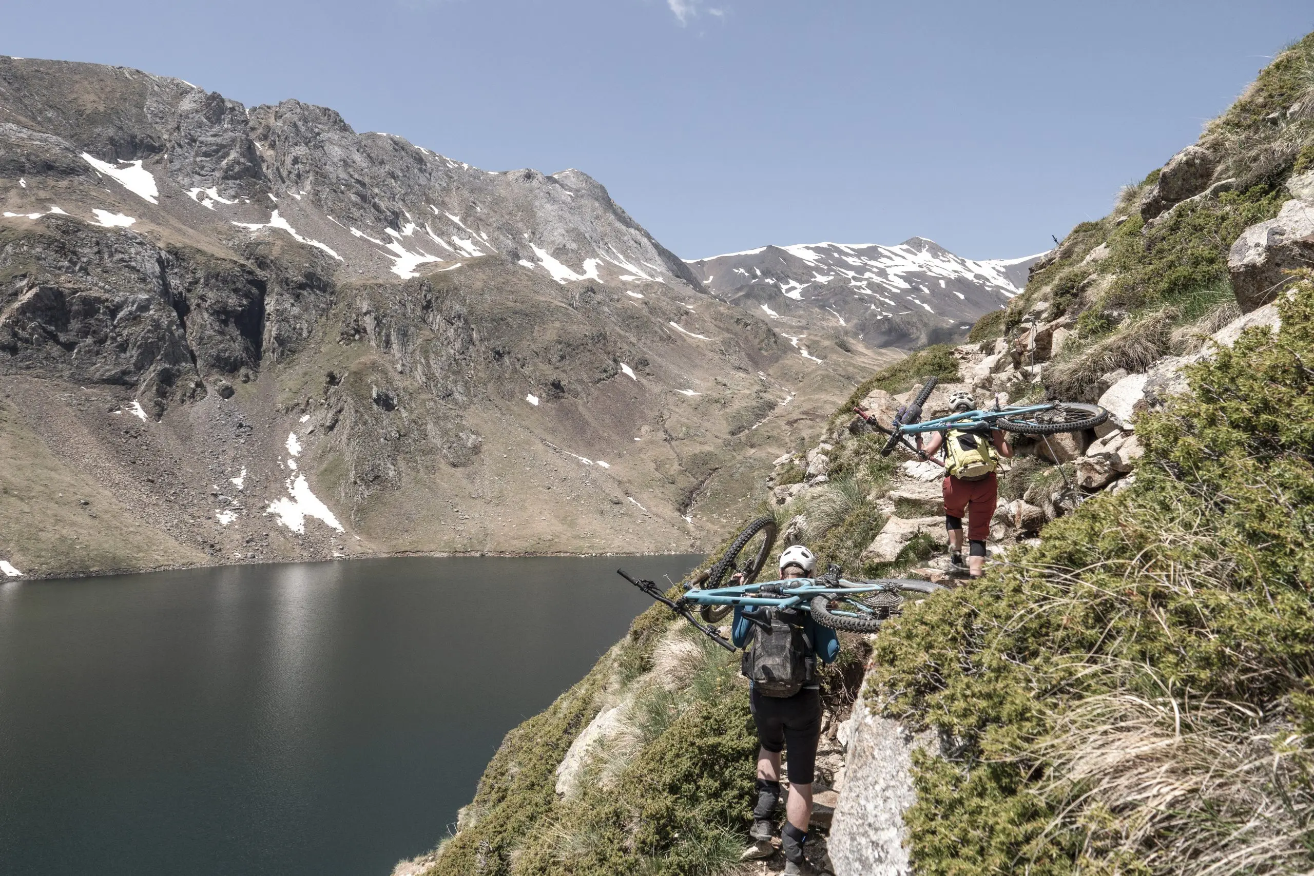 Mountain bikers carry bikes on a steep trail during a Mountain Bike Press Camp, showcasing marketing agency expertise and logistical support. LOAM.