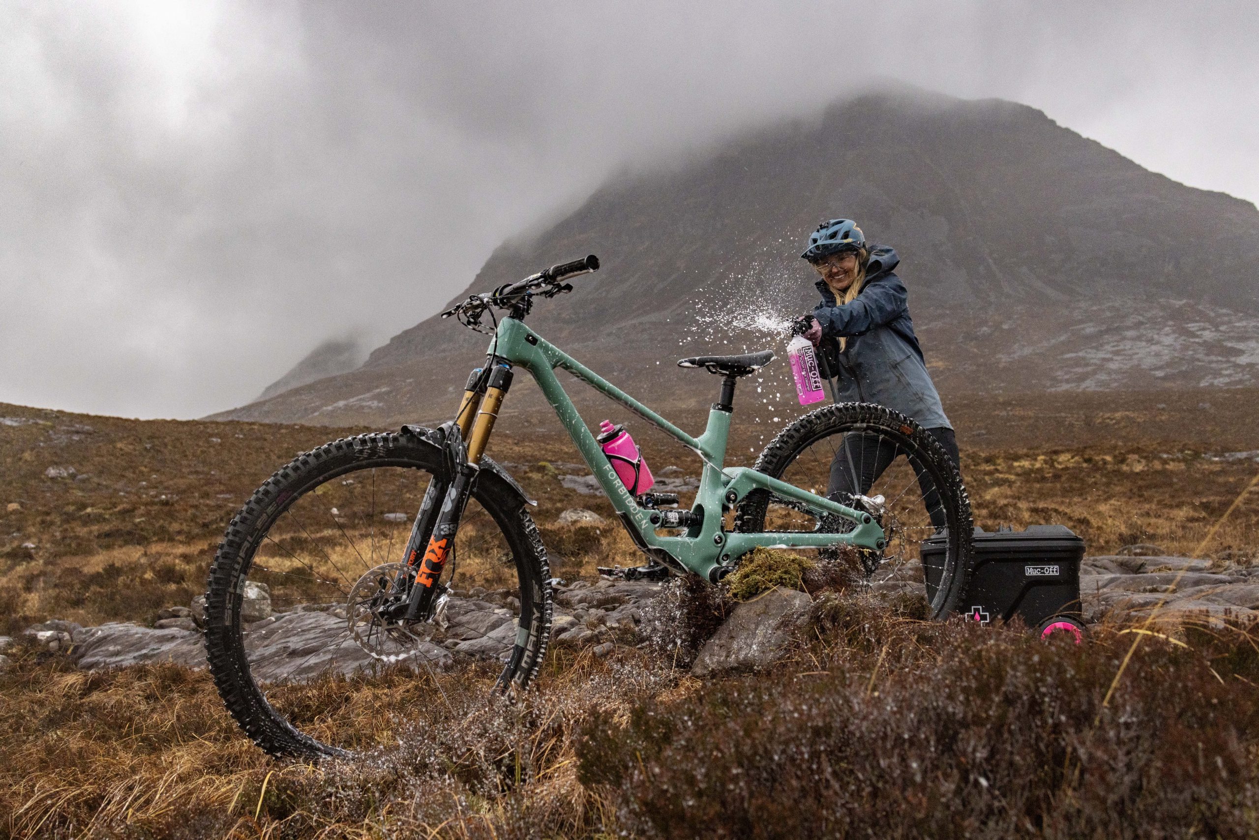 Mountain biker using Muc-Off Mobile Pressure Washer for event planning support in rugged terrain. Ideal for marketing and logistical support needs. LOAM.